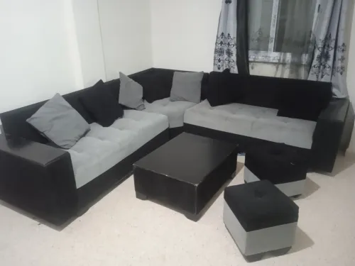 Salon L avec une table et deux poufs. 